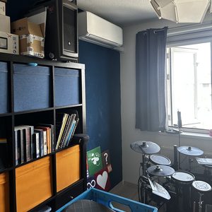 De foto toont een wandairconditioningsunit gemonteerd in een kamer, boven een boekenplank en naast een raam.