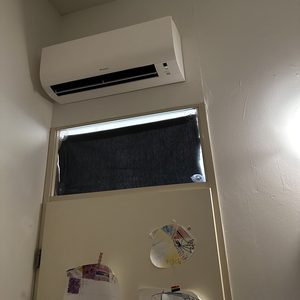 Een wandairco-installatie geplaatst boven een deur, met zichtbare bedieningselementen.