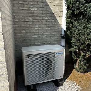 Een luchtverwarmingsunit van Daikin geïnstalleerd aan de buitenzijde van een woning, geplaatst op stevige ondergrond.