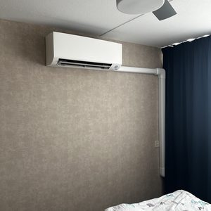 Een luchtconditioningsunit geïnstalleerd aan de wand in een slaapkamer, met een plafondventilator zichtbaar op de achtergrond.