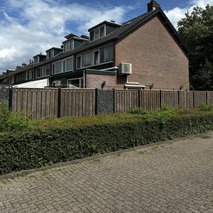 Een airconditioningcompressor is geïnstalleerd aan de buitenzijde van een woning, zichtbaar naast de gevel.