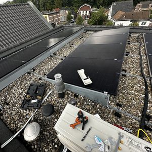 De afbeelding toont een installatie van zonnepanelen op een dak, met gereedschap en bevestigingsmaterialen zichtbaar.