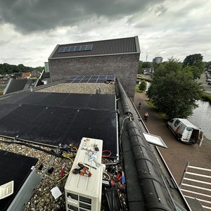 Deze afbeelding toont een airco-installatie op een dak, met zonnepanelen op de achtergrond. De installatie bevat leidingen en aansluitingen.
