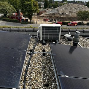 Een airconditioninginstallatie op een dak, omlijst door zonnepanelen en grind. De installatie is zichtbaar in een bouwomgeving.