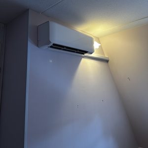 Een wandmontage airconditioningseenheid, geïnstalleerd in een kamer. De unit is uitgerust met twee ventilatieroosters.