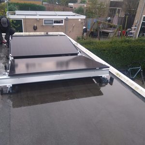 Twee zonnepanelen worden geïnstalleerd op een plat dak, met een technicus die de bevestiging uitvoert.