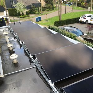 Een reeks zonnepanelen zijn geïnstalleerd op een plat dak, zichtbaar met bevestigingsmateriaal en waterreflecties op het oppervlak.