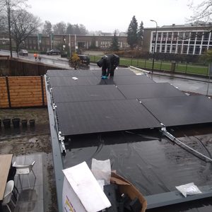 De foto toont een installatie van zonnepanelen op een dak, met een technicus die de panelen aanbrengt.